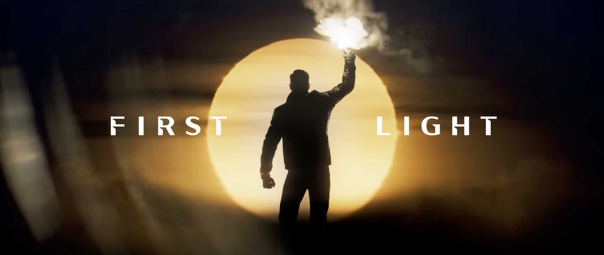 A silhouette of a person holding a bright flare stands before a large, glowing sun, evoking the cinematic style of a Game Title Sequence with the words “FIRST LIGHT” on either side. Frame from Stash Magazine article.