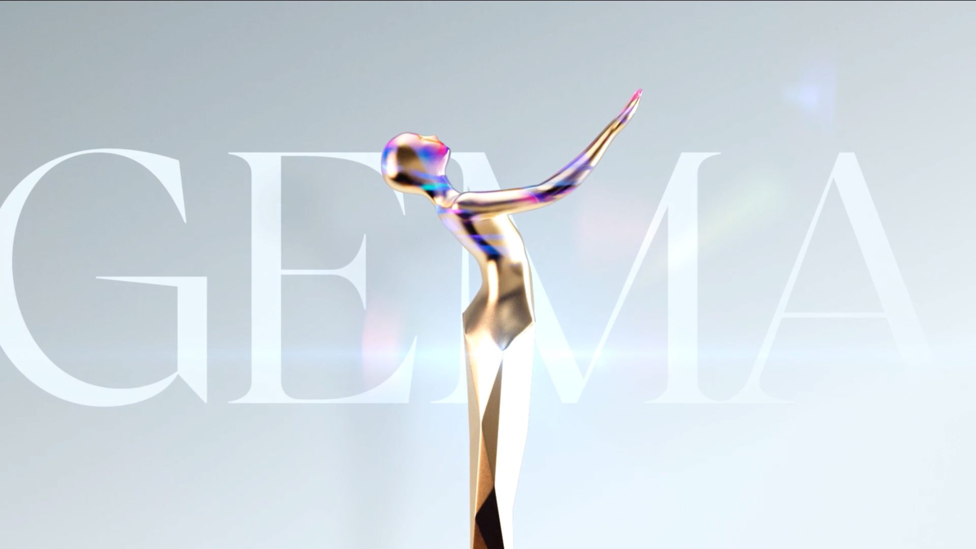 A shiny, abstract gold sculpture of a figure with arms raised stands before large, translucent letters spelling GEMA on a light background, celebrating the GEMA Awards. Frame from Stash Magazine article.