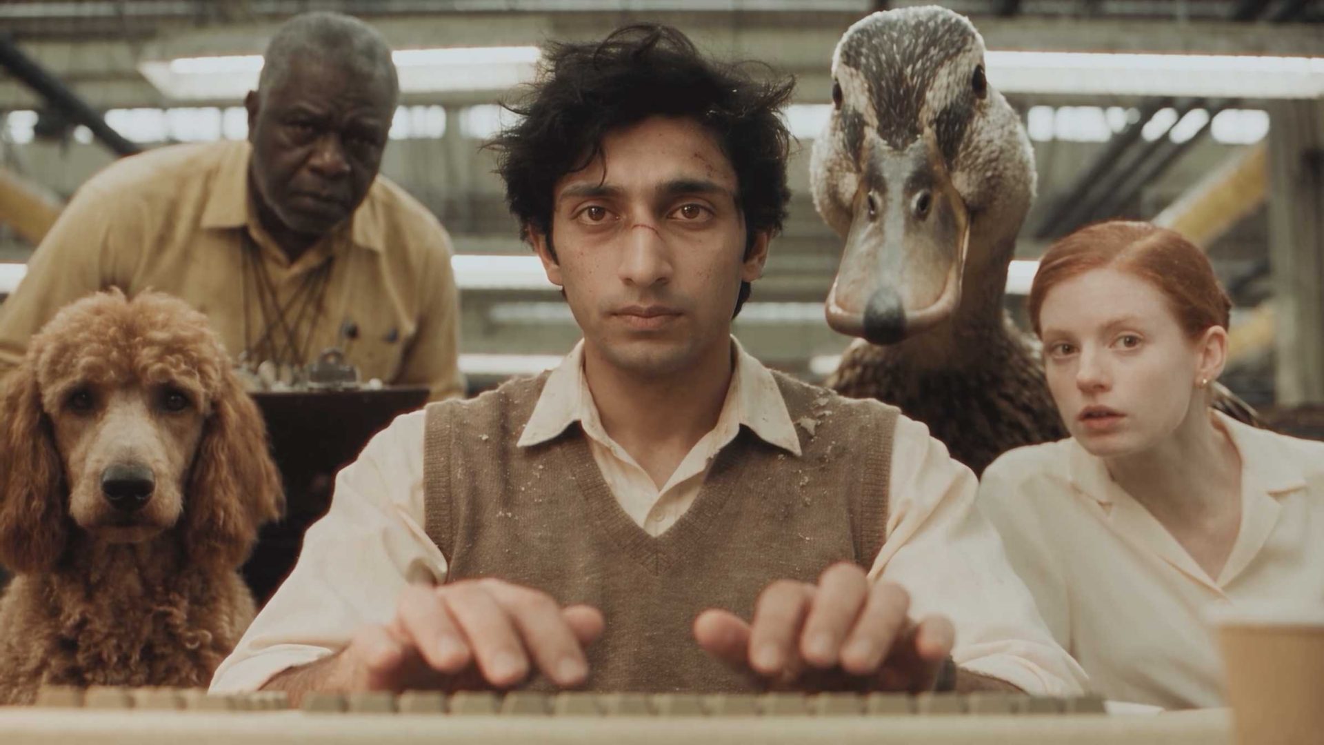 A man types at a computer in a scene from the short film Query, surrounded by a poodle, an older man, a duck, and a woman. Frame from Stash Magazine article.