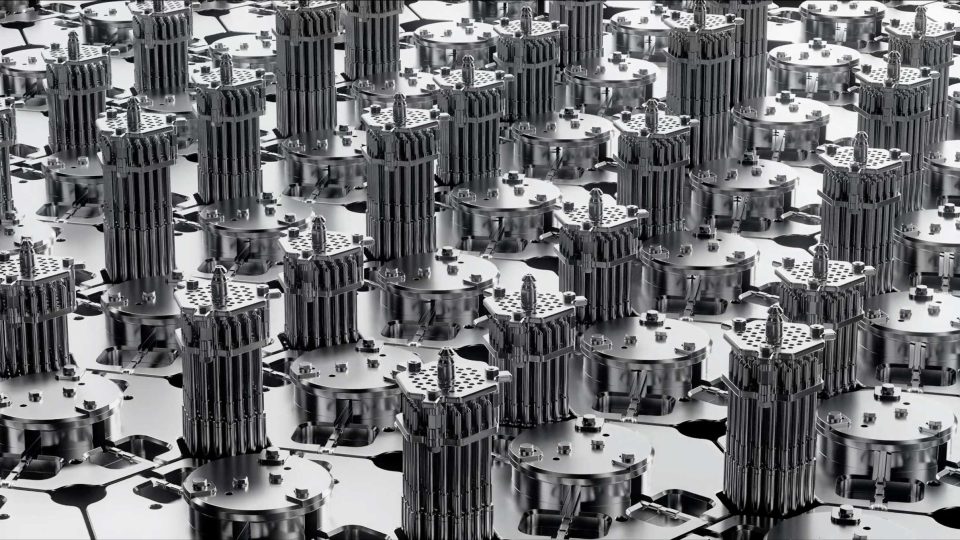 Rows of futuristic, metallic tower-like structures with intricate details, arranged closely together on a reflective surface, create a geometric, industrial pattern reminiscent of the visionary aesthetics seen in Aalo Atomic Energy Without Limits brand film by Stylo Creative. Frame from Stash Magazine article.