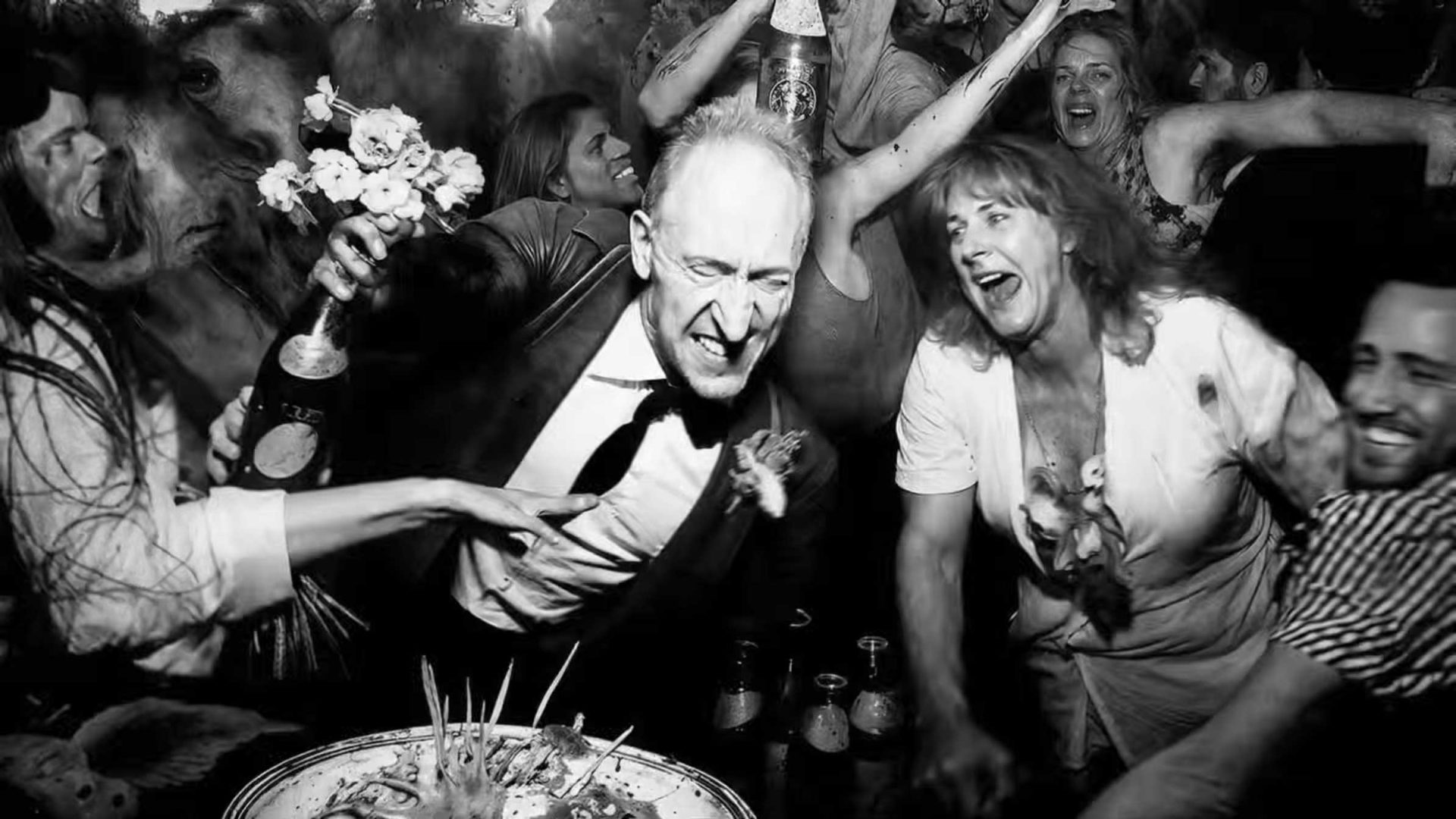 A lively black-and-white party scene reminiscent of Alessandro Bavari's visual style, with people dancing, laughing, and holding drinks. A man in a suit and a woman in a white shirt are joyfully celebrating near a table with a partially eaten cake, evoking the dynamic energy of the Solid Light From Space SHORT FILM. Frame from Stash Magazine article.