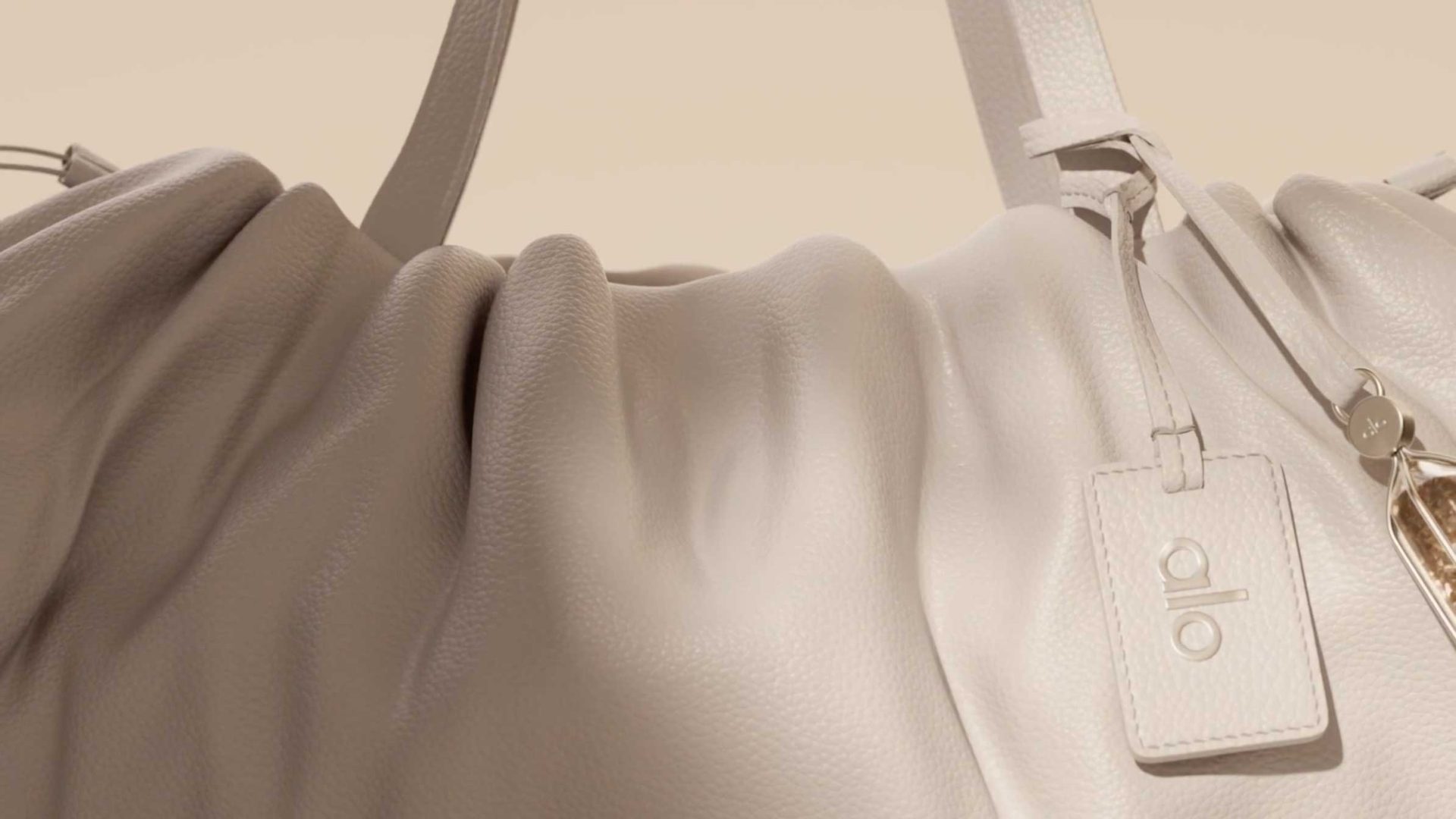 Close-up of a light-colored, gathered Alo handbag with a brand tag hanging from the strap, embodying a sense of quiet luxury. Frame from Stash Magazine article.