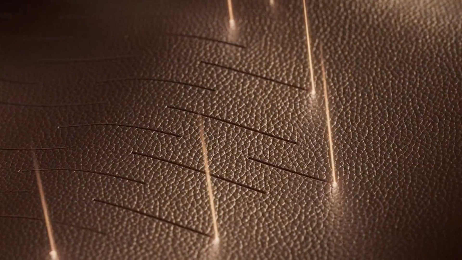 A laser cuts a Tendril Intro pattern of thin, segmented lines into a sheet of textured brown material for Alo Handbags. Frame from Stash Magazine article.