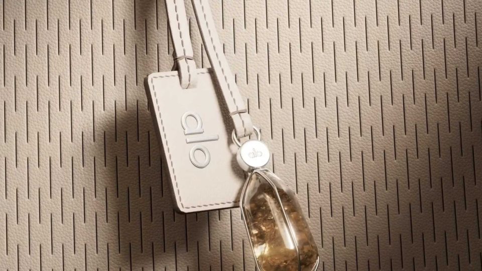 Beige Alo handbag with a perforated surface, featuring an Alo-branded luggage tag and a decorative stone charm, as seen in films by Tendril. Frame from Stash Magazine article.