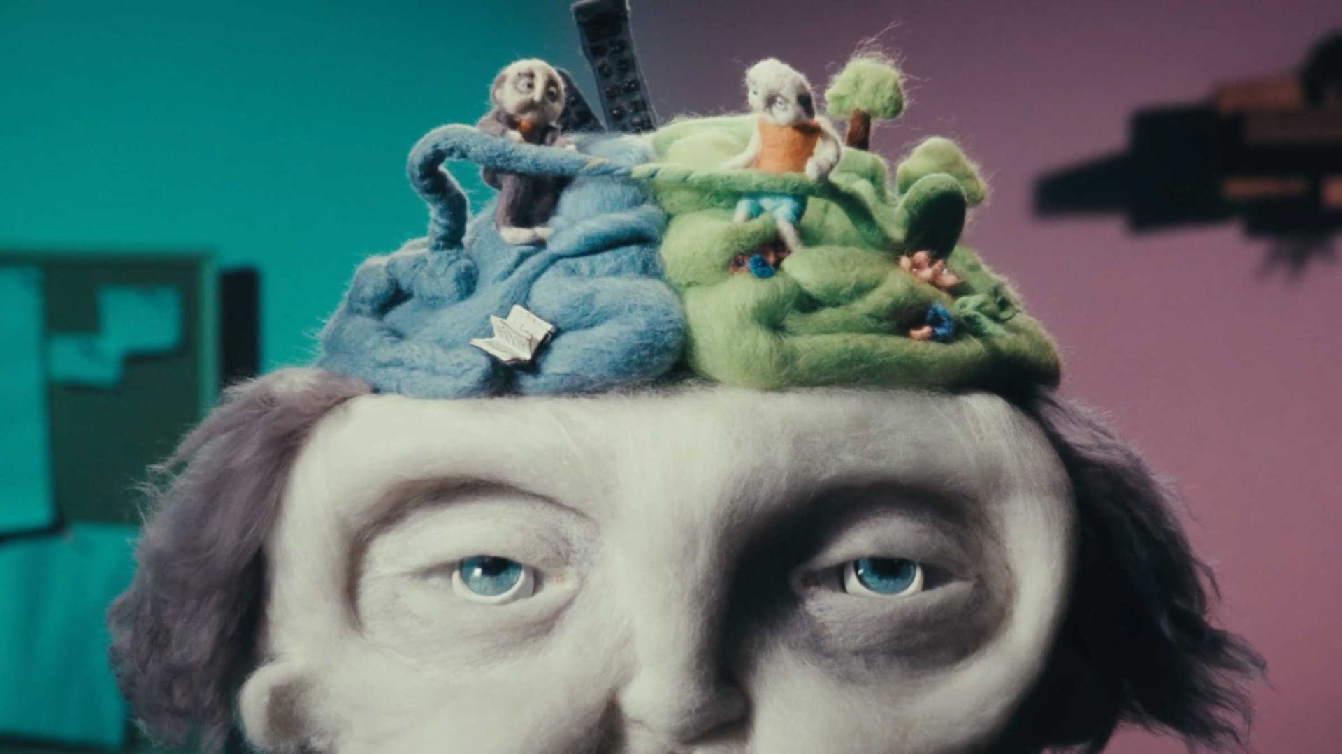 A close-up of a clay figure with a blue and green felt landscape on its head, depicting a miniature scene inspired by the Paul Jordan Run for Mental Health. Frame from Stash Magazine article.
