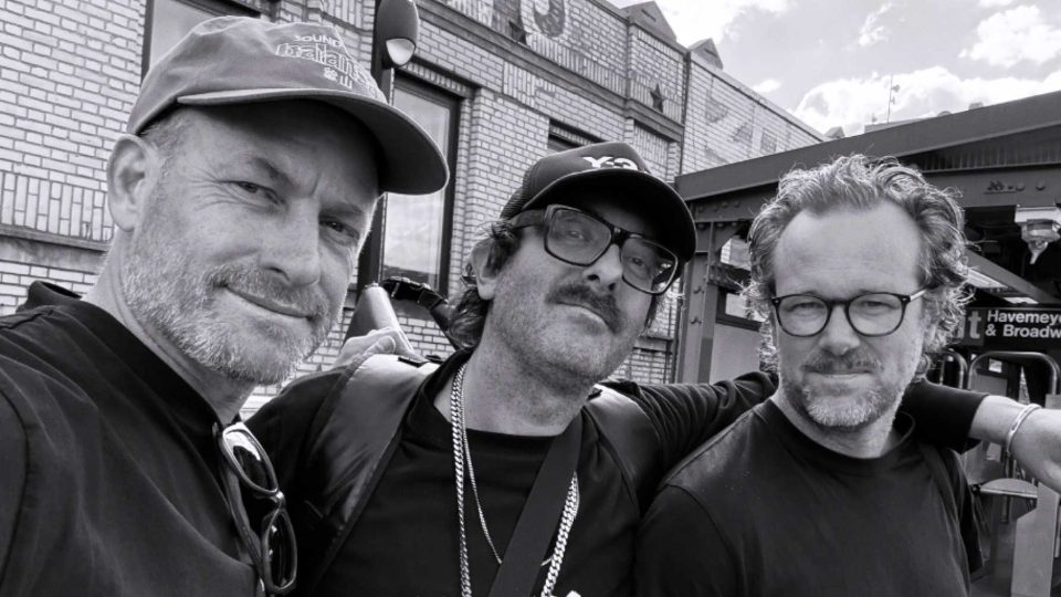 Three men pose closely together for a selfie outside a brick building. All wear glasses; two have facial hair, and one wears a cap. The photo is in black and white, capturing members of Assembly, the award-winning design and animation studio based in Auckland—now celebrating the opening of its first overseas office in New York in 2026. Frame from Stash Magazine article.