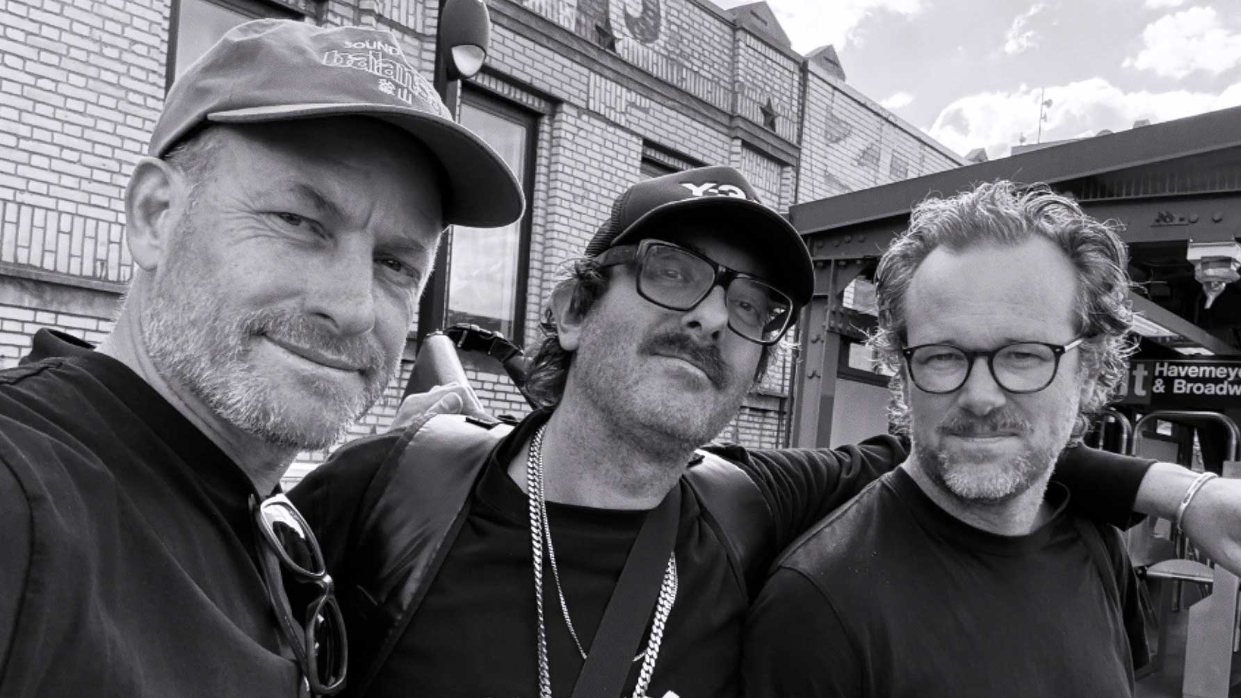 Three men pose closely together for a selfie outside a brick building. All wear glasses; two have facial hair, and one wears a cap. The photo is in black and white, capturing members of Assembly, the award-winning design and animation studio based in Auckland—now celebrating the opening of its first overseas office in New York in 2026. Frame from Stash Magazine article.