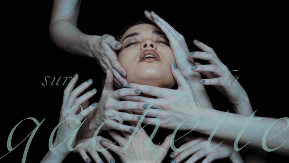 A woman's face with eyes closed is surrounded and touched by many pale hands against a black background. Faint, cursive French text sur la gâchette overlays the image, echoing the ethereal mood of the Bai yun Ici remix music video by Sijin Liu. Frame from Stash Magazine article.