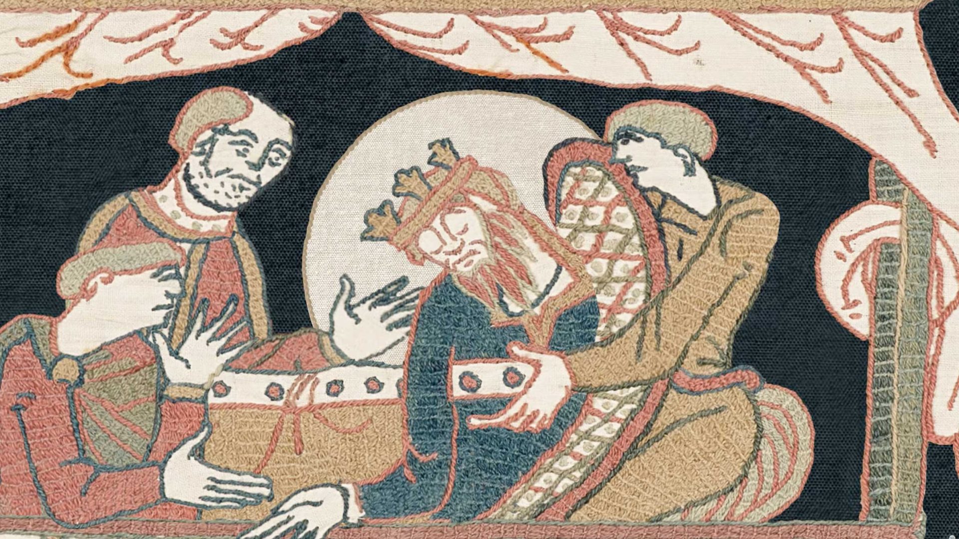 Medieval tapestry, reminiscent of the Bayeux Tapestry, depicting three figures placing a crown on a bearded, crowned man with a halo, who appears to be resting or reclining under a canopy. Frame from Stash Magazine article.