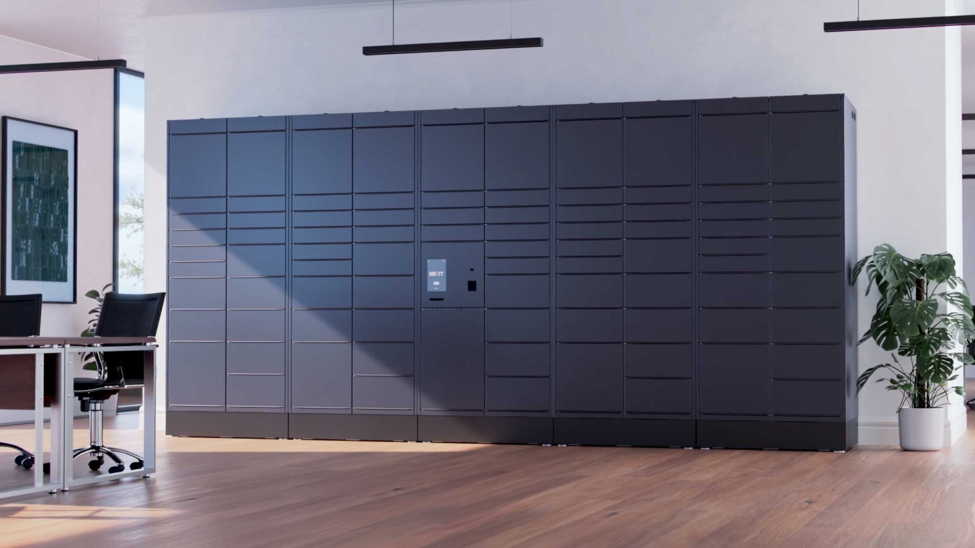 A large, modern, black Bloq.it smart locker system stands against a white wall in a bright, spacious office with wooden floors, two office chairs, and a potted plant nearby—captured with stunning depth of field. Frame from Stash Magazine article.