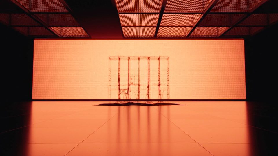 Minimalist scene with an orange glow, featuring a transparent, cage-like structure at the center, reminiscent of a Bloq.it Smart Lockers product film by Depth of Field. The ceiling’s grid pattern and long shadows enhance the modern, polished space. Frame from Stash Magazine article.