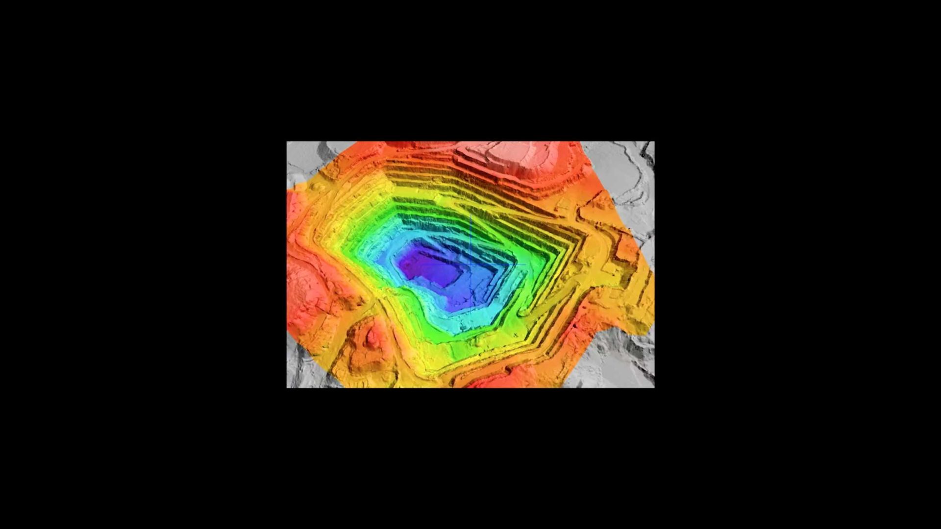 A topographic map featuring a multicolored open-pit mine, with contour lines transitioning from red and orange to blue and purple—like visuals from a Bonobo "Me And You" music video—indicating elevation changes. Frame from Stash Magazine article.