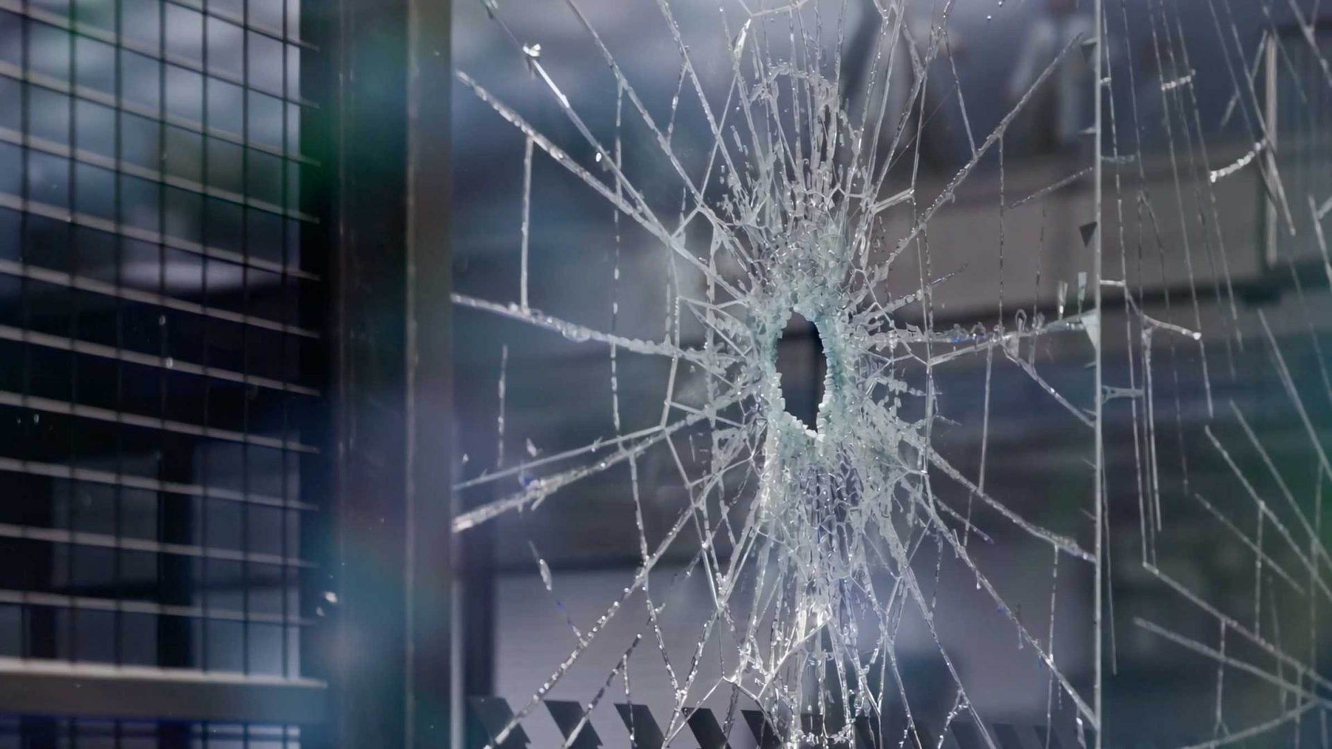A circular bullet hole in a pane of reinforced wire glass, with fractures radiating outward like the impact pattern of a Kutuko or Bullpadel Xplo 02. Frame from Stash Magazine article.