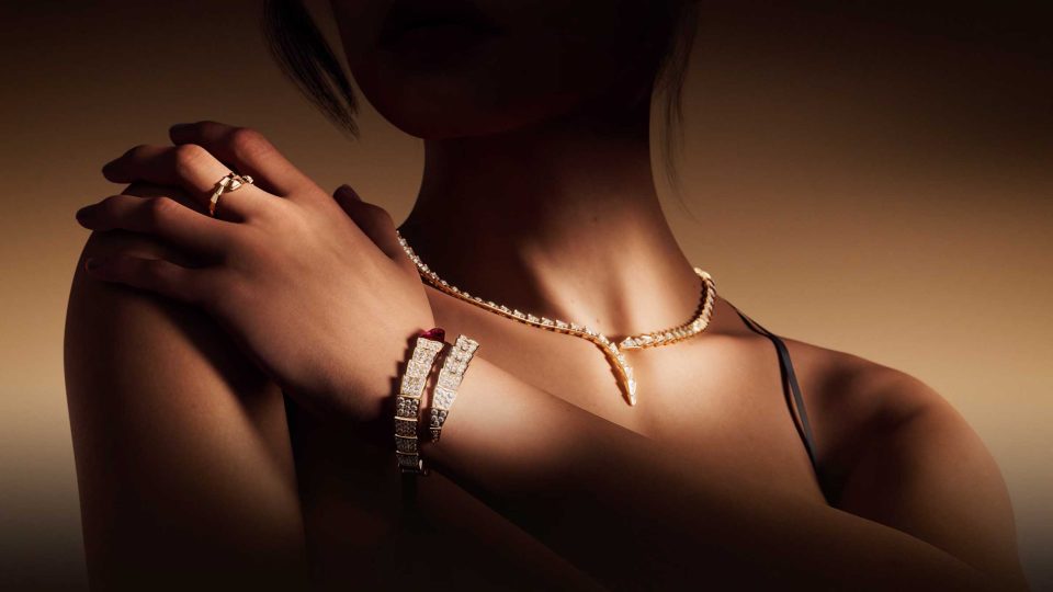 A woman with crossed arms wears a diamond necklace, matching bracelet, and a ring. Soft lighting highlights the jewelry against her skin, with the background fading into a warm gradient, evoking the luxurious allure of a Bvlgari Serpenti Spec Spot by Vladislav Evdokimov. Frame from Stash Magazine article.