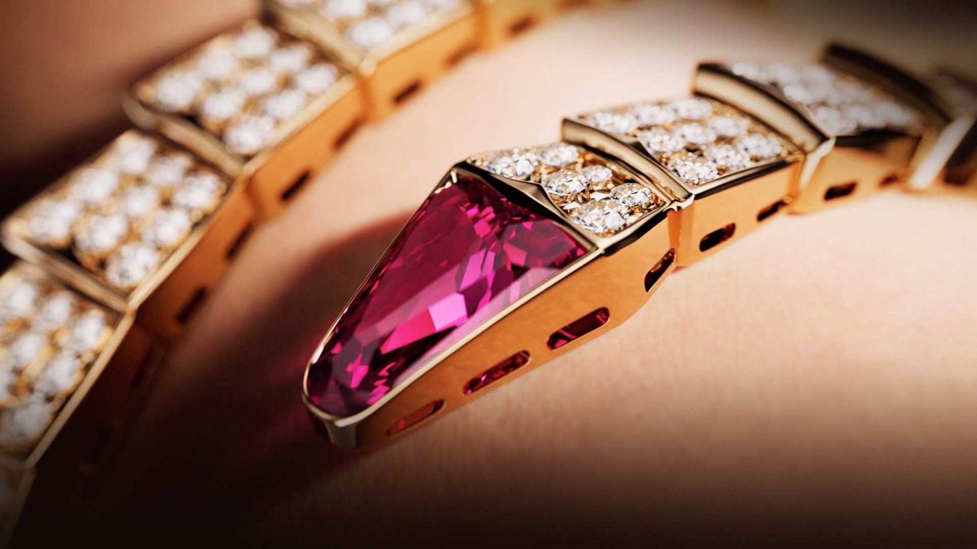 Close-up of a gold bracelet in the style of Bvlgari Serpenti, featuring a large, faceted pink gemstone and segments set with small sparkling diamonds, shown against a blurred background reminiscent of Spec Spot photography by Vladislav Evdokimov. Frame from Stash Magazine article.