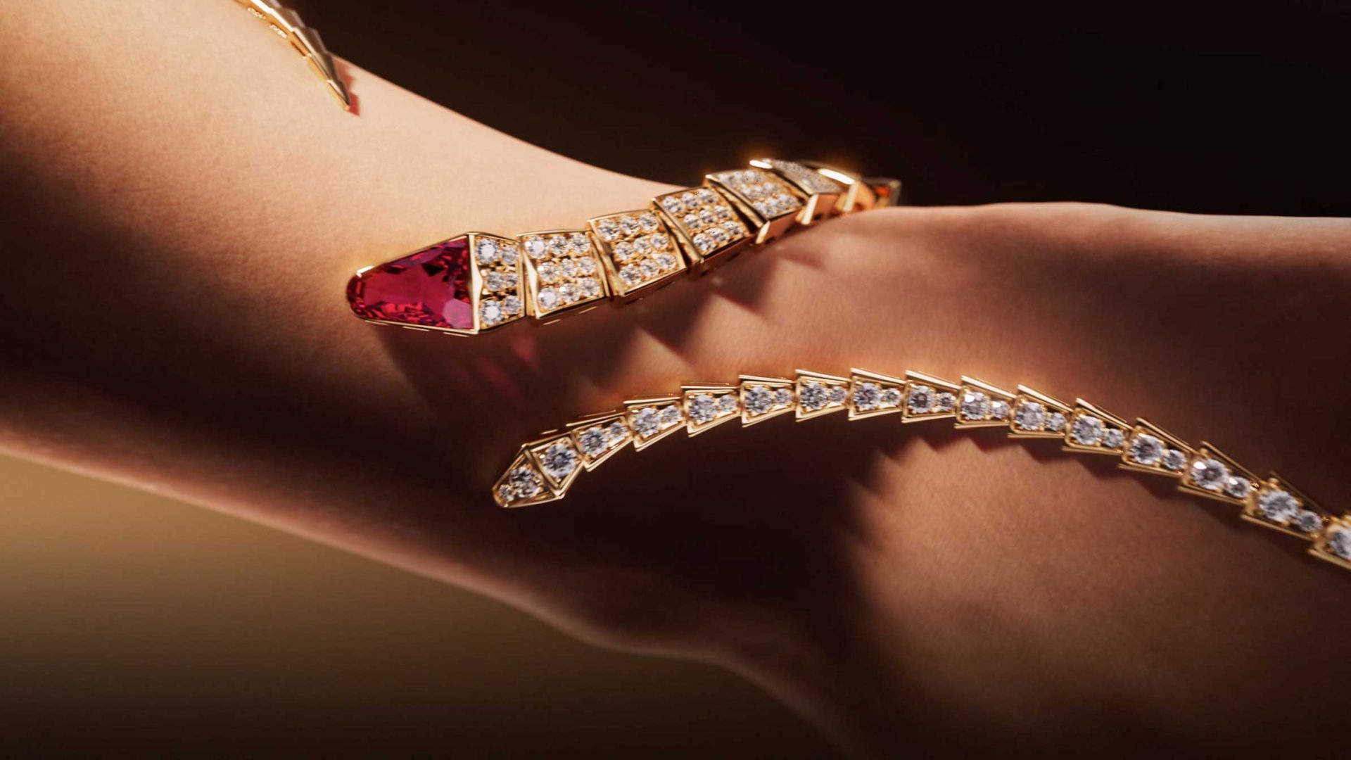 A gold, snake-inspired bracelet with diamond segments and a ruby-like gem on the head wraps elegantly around a person's arm, echoing the iconic allure of Bvlgari Serpenti designs featured in Spec Spot by Vladislav Evdokimov. Frame from Stash Magazine article.