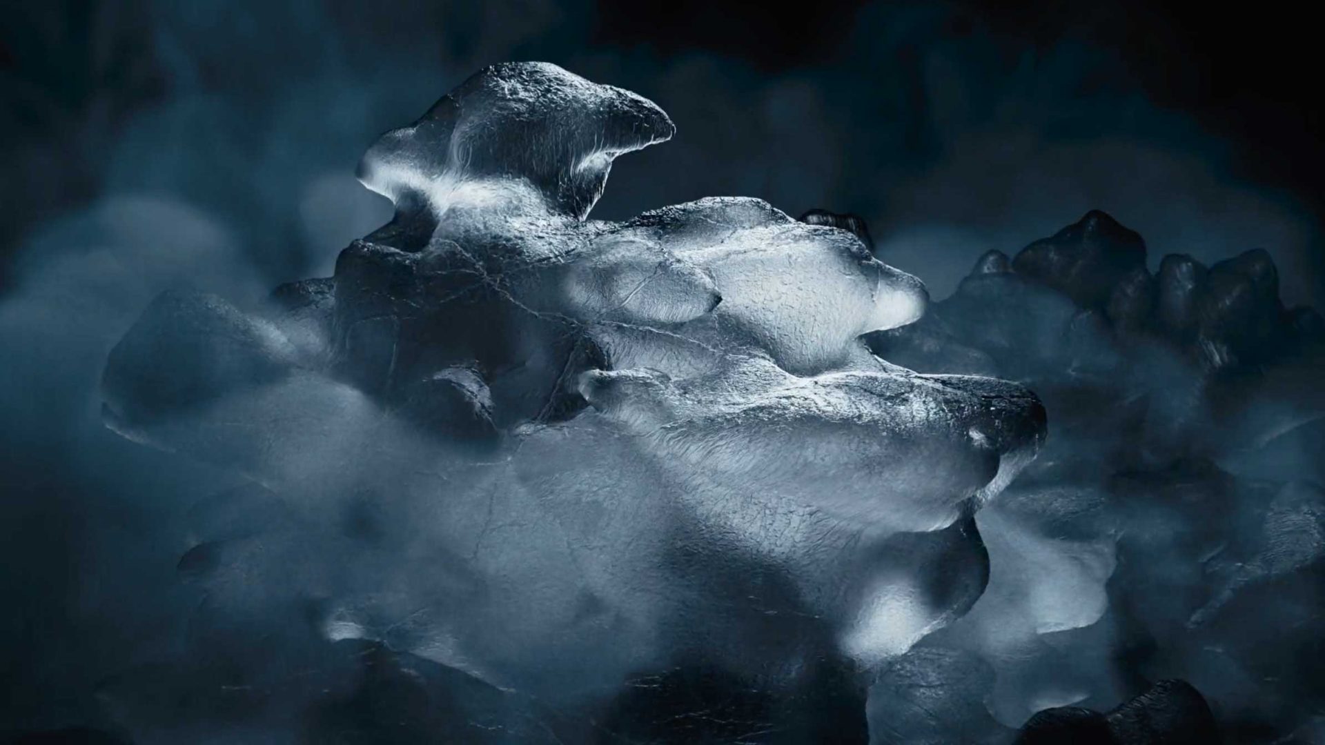 A large, irregularly shaped chunk of ice glows softly against a dark, misty background, with fog swirling around its smooth and jagged surfaces—like a CCM Jetspeed skate featured in a Freek Freriks commercial. Frame from Stash Magazine article.