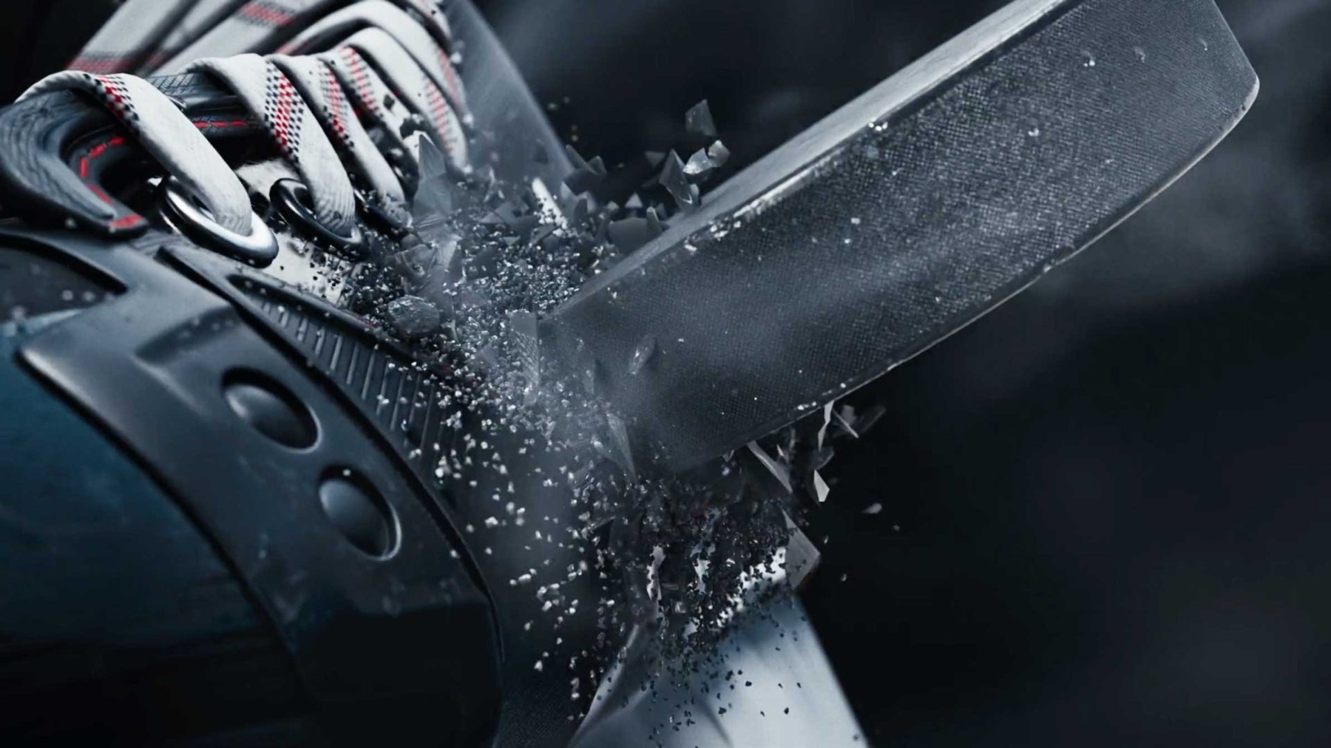 Close-up of a CCM Jetspeed hockey puck shattering as it strikes the front of a skate, with pieces flying off in all directions and laces visible—capturing thrilling commercial action. Frame from Stash Magazine article.