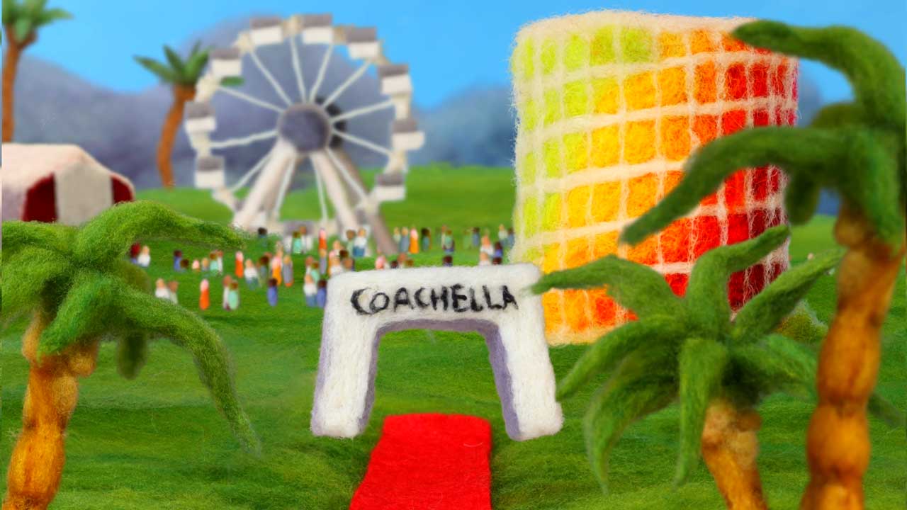 A felt art scene of Coachella 2026 with palm trees, a red carpet, a sign reading Coachella, colorful tower, Ferris wheel, and a crowd of tiny felt people on a grassy field under a blue sky—brought to life in Andrea Love’s charming style. Frame from Stash Magazine article.