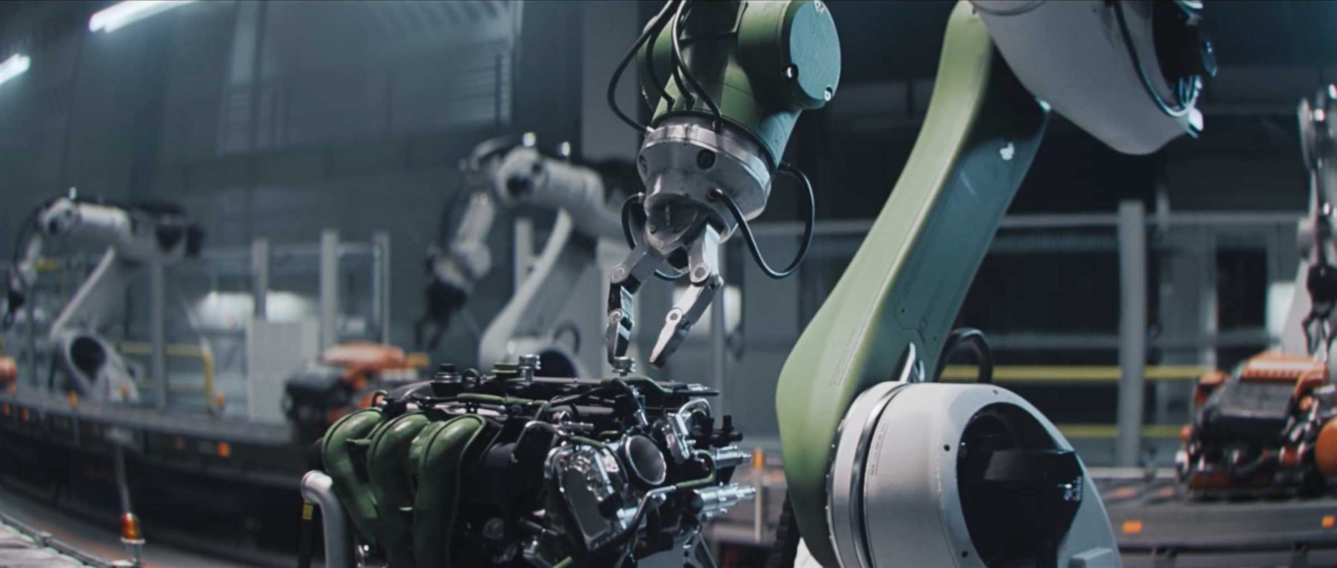 Robotic arms assemble machinery parts in an industrial factory setting, echoing the precision and dynamic choreography seen in the Dacia Robots commercial by Romain Chassaing, with particular focus on one robotic arm working meticulously on a complex engine component. Frame from Stash Magazine article.