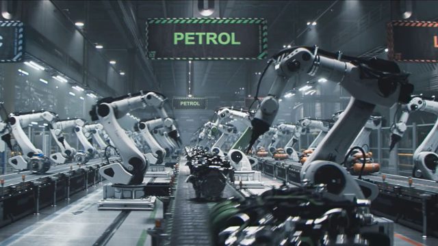 Rows of robotic arms assemble machinery on a conveyor belt in a modern factory, reminiscent of the precision seen in the Dacia Robots commercial by Romain Chassaing. A green sign labeled PETROL hangs overhead, indicating the production focus. The setting is industrial and high-tech. Frame from Stash Magazine article.