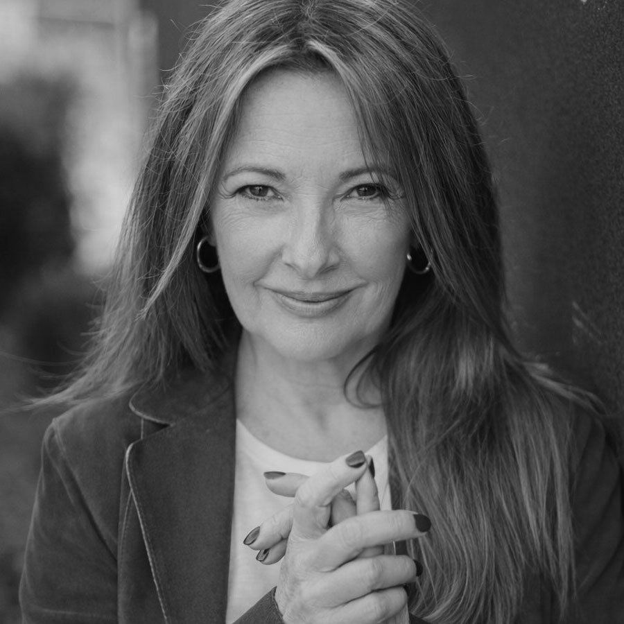 Black and white portrait of a middle-aged woman with long hair, wearing a blazer and hoop earrings, smiling gently and clasping her hands—panelist for "Breaking Through: Getting Seen & Getting Results" at OFFF Barcelona 2026. Frame from Stash Magazine article.
