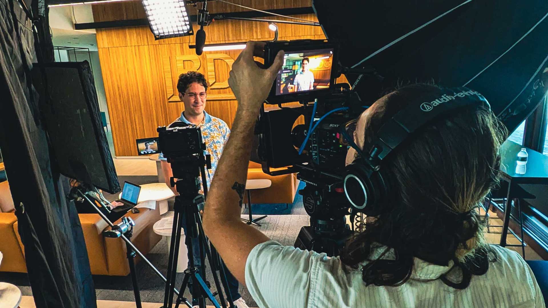A videographer filming a man during an interview as part of Demo Duck’s long-form documentary videos services in a modern office. Frame from Stash Magazine article.