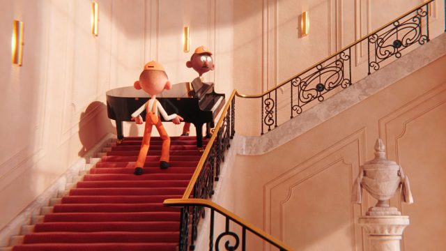 Two animated characters in orange uniforms carry a grand piano up a red-carpeted staircase with ornate railings in this comic film by Léo Brunel. One character leads the duet, while the other struggles behind in a grand, well-lit interior. Frame from Stash Magazine article.