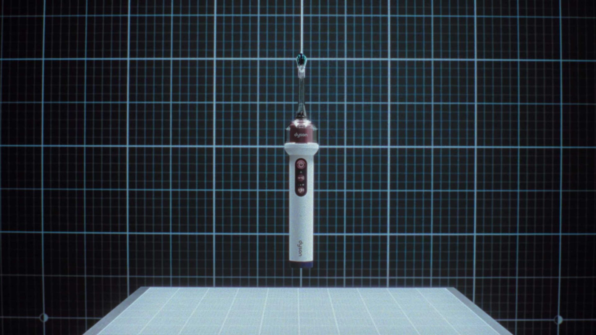 A white and brown Dyson CameraJet handheld device hangs vertically by a thin wire against a blue grid background, with a grid-patterned surface below—a scene reminiscent of Will Dohrn’s visual storytelling in “Love Song.”. Frame from Stash Magazine article.