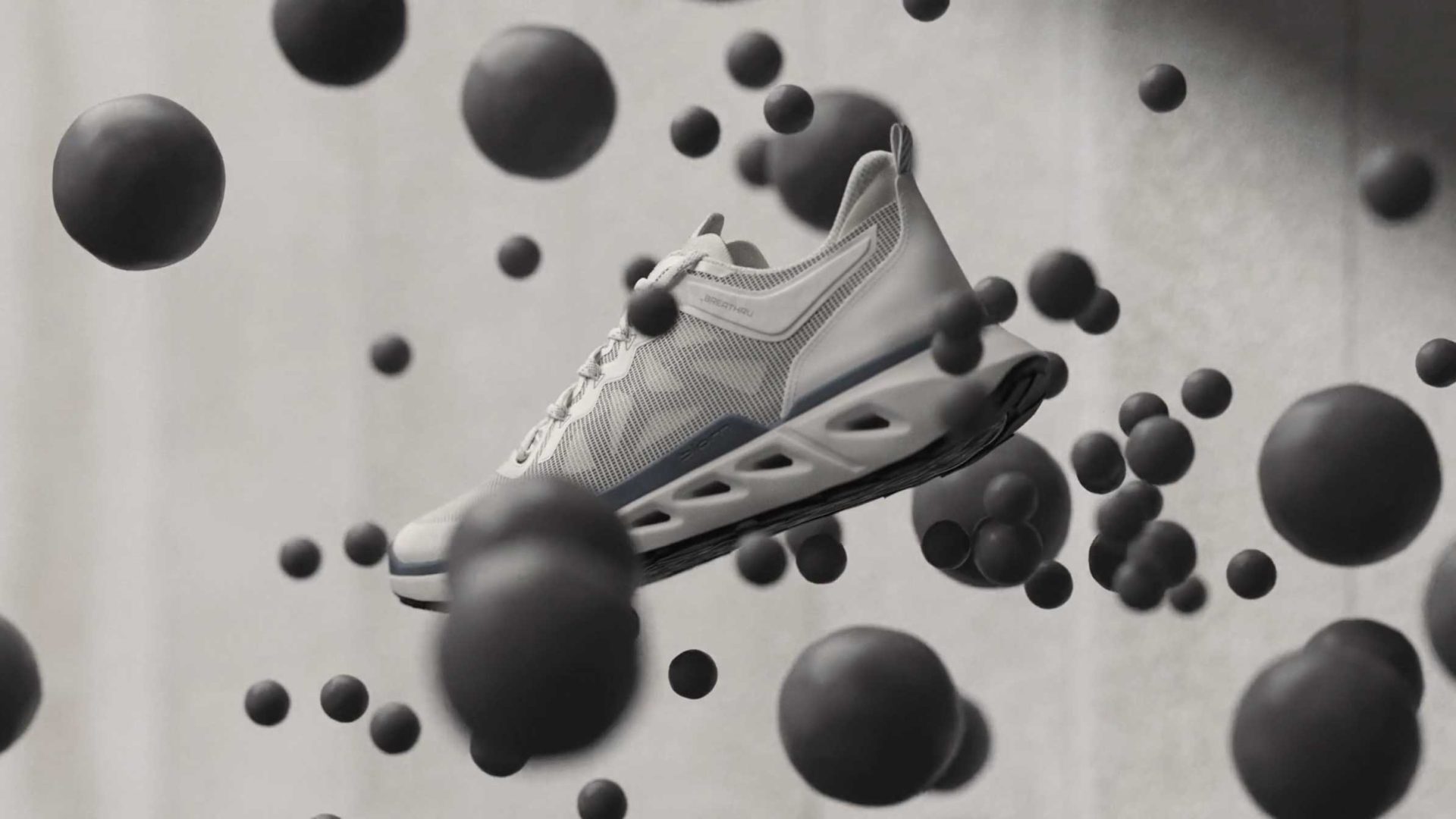 A white athletic sneaker, the ECCO Biom 720, with a thick, sculpted sole is suspended in midair, surrounded by floating black spheres against a blurred, neutral background—perfect for your next product film. Frame from Stash Magazine article.