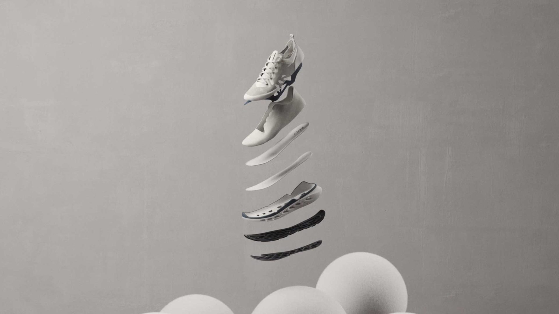 A white ECCO Biom 720 sneaker is shown in mid-air, separated into its individual layers, displaying the sole, insole, and upper components. The gray background features three white spheres at the bottom, evoking a minimalist product film by KORB. Frame from Stash Magazine article.