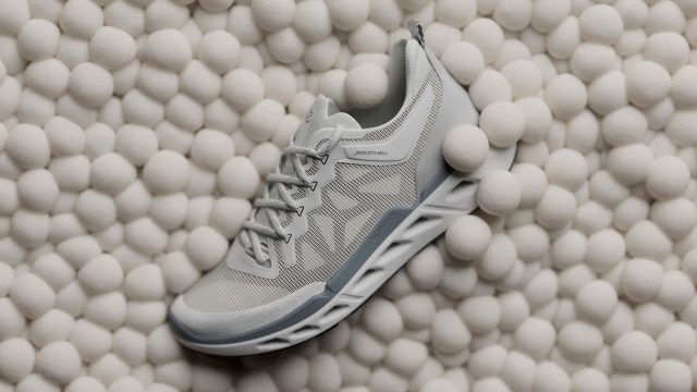A light gray ECCO Biom 720 sneaker with a textured sole rests on a surface covered in small, white, round balls. The shoe features mesh fabric and lace-up closure, as seen in the ECCO Biom 720 Product Film by KORB. Frame from Stash Magazine article.