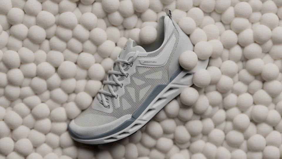 A light gray ECCO Biom 720 sneaker with a textured sole rests on a surface covered in small, white, round balls. The shoe features mesh fabric and lace-up closure, as seen in the ECCO Biom 720 Product Film by KORB. Frame from Stash Magazine article.