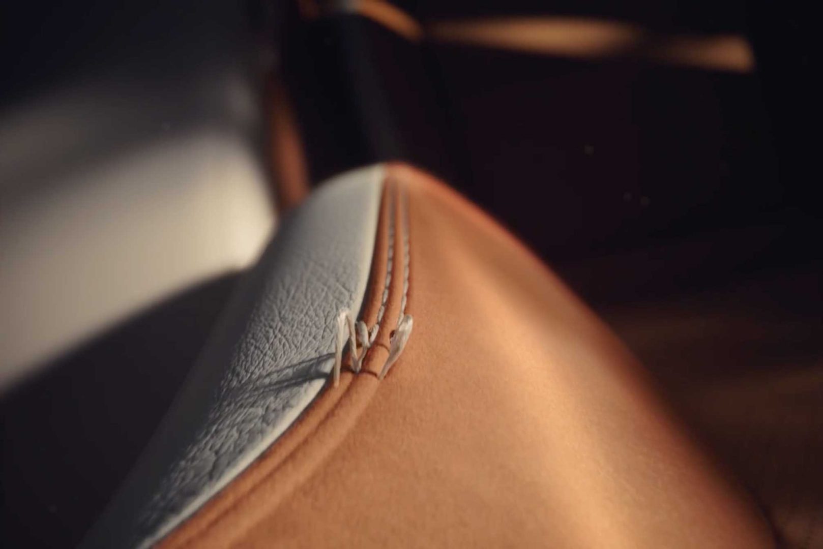 Close-up of a car seat with textured white and smooth tan leather, detailed stitching, and a zipper between materials—sunlight highlights contours as Electrical Theatre Collective digs into the "Details" of Lexus RZ craftsmanship. Frame from Stash Magazine article.