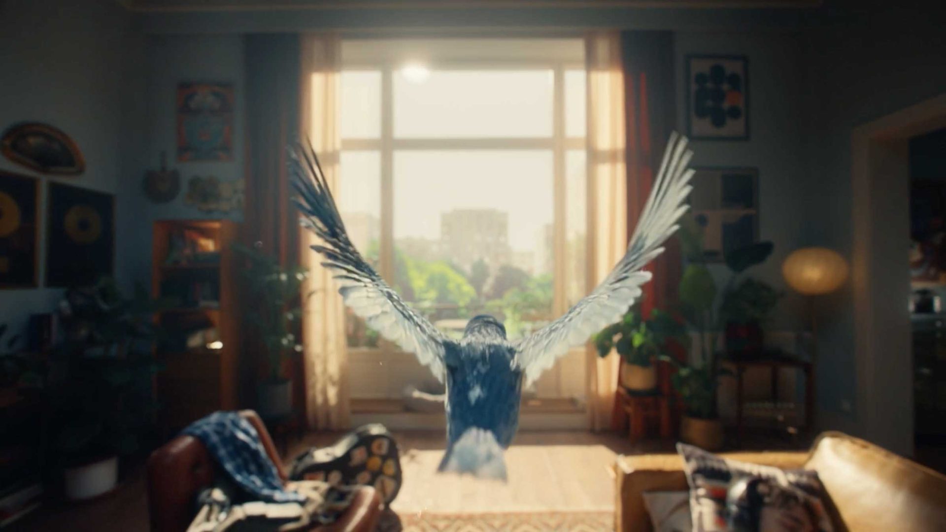 A blue bird, inspired by The Bird series, with outstretched wings flies toward a sunlit window in a cozy living room filled with plants, sofas, and framed artwork, with sunlight streaming into the space. Frame from Stash Magazine article.
