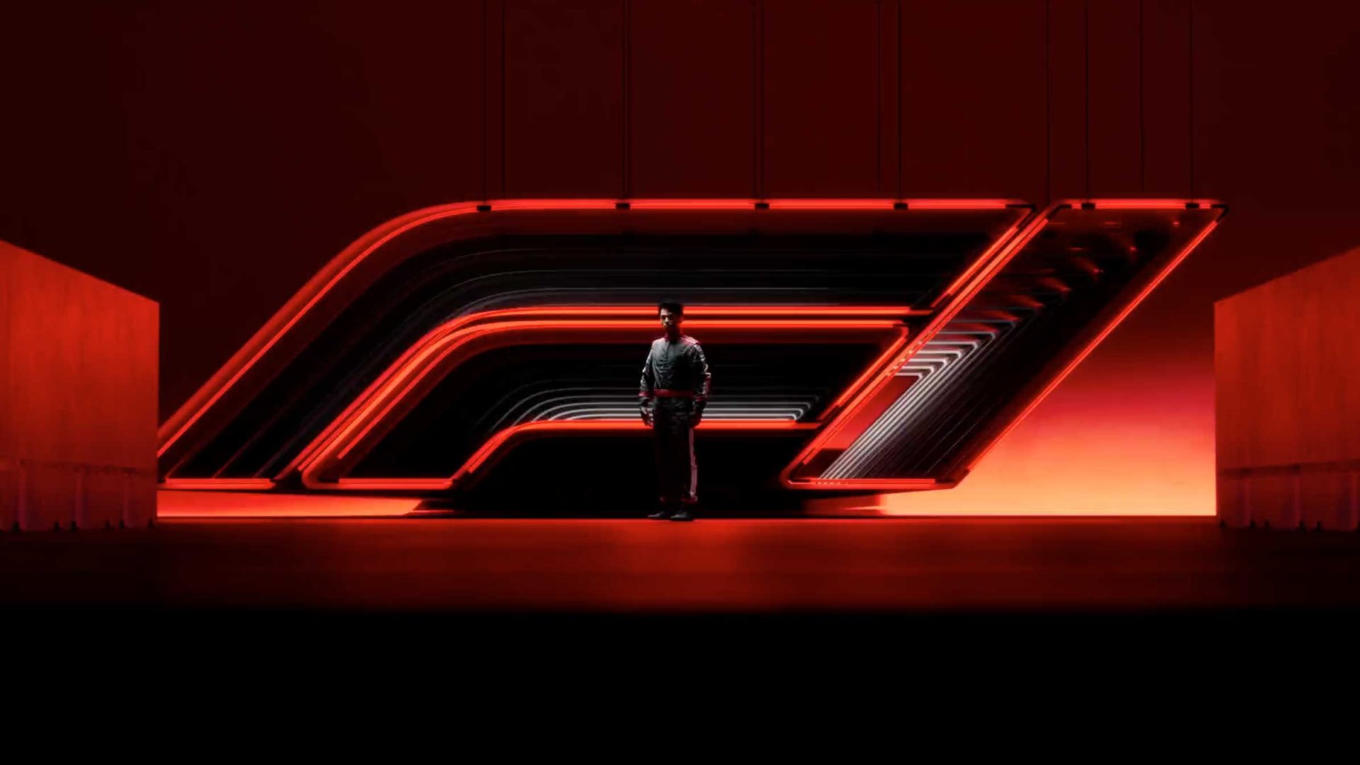A person stands in front of a large, illuminated Formula 1 logo, glowing red and black in a dark, dramatic setting. The futuristic atmosphere hints at the transformative process leading to F1 2026. Frame from Stash Magazine article.