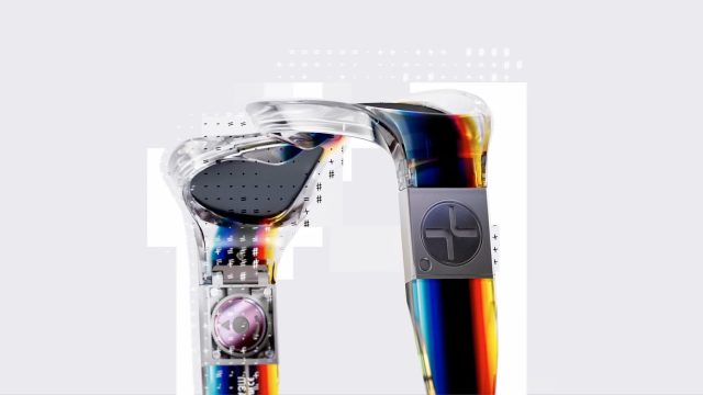 Two transparent, futuristic ear-worn devices from the Felipe Pantone x Etnia Barcelona brand film with visible internal components and a rainbow-gradient finish. Frame from Stash Magazine article.