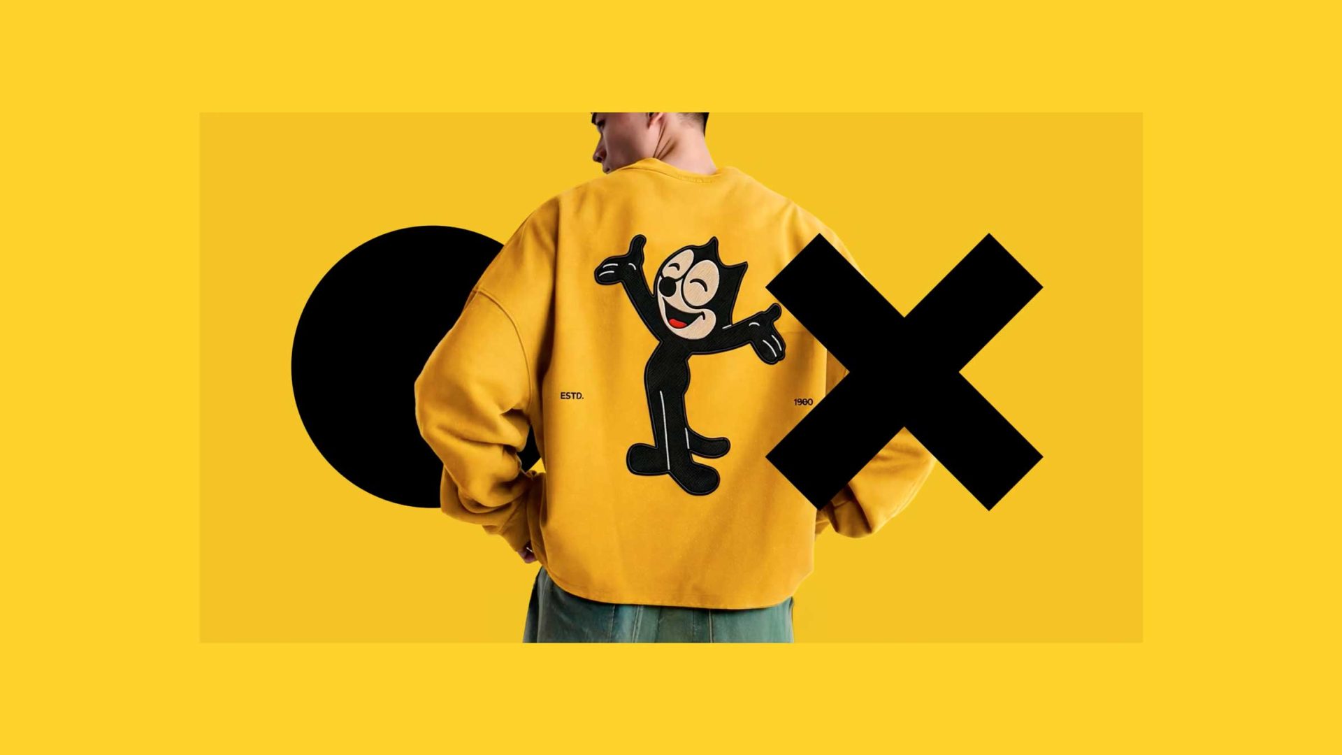 A person facing away wears a yellow jacket featuring Felix the Cat. Large black geometric shapes—a circle and an X—overlay the image on a bright yellow background, capturing Soda Creative’s vibrant style in this sizzle reel-inspired scene. Frame from Stash Magazine article.