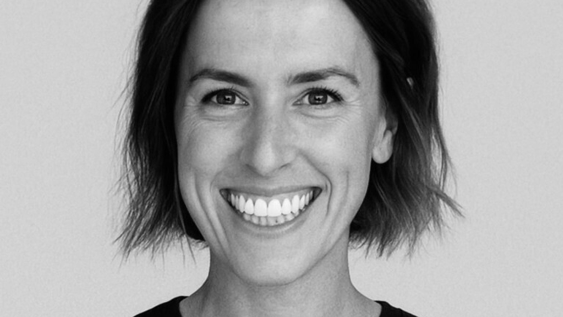 A woman with short, dark hair smiles widely at the camera against a plain, light background. She is wearing a dark top, radiating confidence befitting her role as VP Client Partnerships. This is Carolyn Taylor—her warm expression capturing the commitment she brings to Forever. Frame from Stash Magazine article.