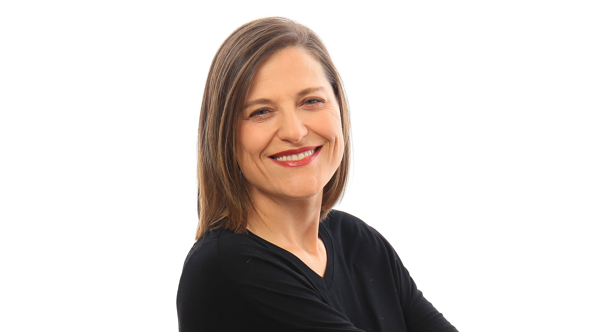 Woman with straight brown hair, wearing a black top, smiling with arms crossed against a plain white background—announcing FutureDeluxe appoints Mercedes Perez-Bode as Business Director. Frame from Stash Magazine article.
