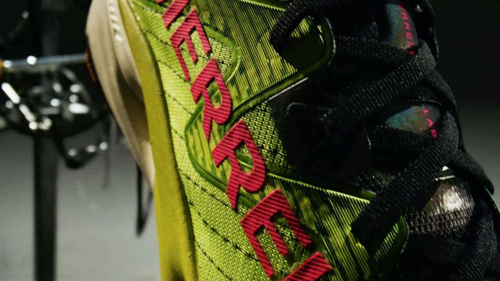 Close-up of a green and yellow Merrell athletic shoe with black laces and bold red MERRELL branding on the side, showcasing the innovative design of the MTL SpeedARC Peak. Frame from Stash Magazine article.