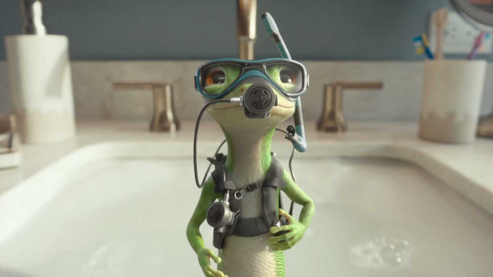 A cartoon GEICO Gecko wearing scuba gear and goggles stands in front of a bathroom sink, ready for some deep diving, with faucets and toiletries visible in the background. Frame from Stash Magazine article.