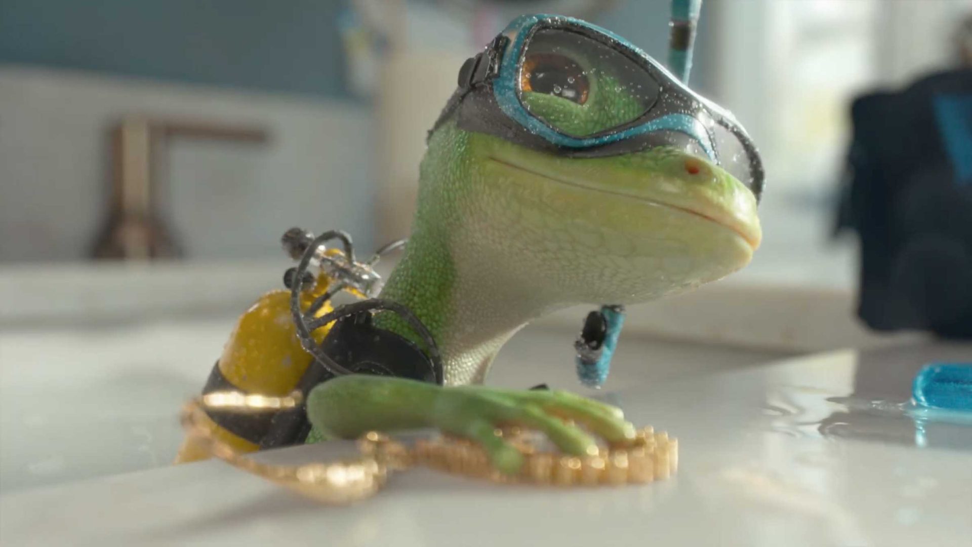 A small animated GEICO Gecko, expertly crafted by Framestore, is sporting scuba gear—including a mask and snorkel—as it goes deep diving in a sink while clutching a gold necklace. Water droplets glisten on its face and goggles, highlighting its adventurous spirit. Frame from Stash Magazine article.