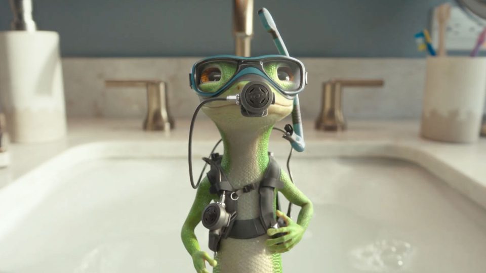 A cartoon gecko wearing scuba gear, including goggles, a snorkel, and an oxygen tank, stands on the edge of a sink with a bathroom faucet and counter visible in the background—just like the GEICO Gecko Dive commercial with VFX by Framestore. Frame from Stash Magazine article.