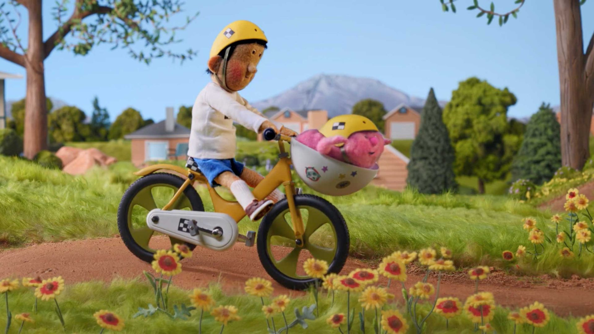 A claymation figure of a child wearing a yellow helmet rides a yellow bicycle on a dirt path, carrying a pink stuffed animal in a helmet-mounted basket. Inspired by Anna Mantzaris, the scene captures the spirit of Take Your Brain Out in Colorado’s great outdoors. Frame from Stash Magazine article.