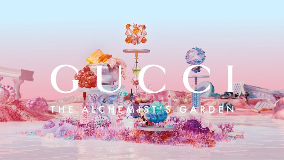 Colorful, surreal landscape with crystal-like structures and flowers against a pastel blue and pink background. Large white text reads GUCCI and below, THE ALCHEMISTS GARDEN, inspired by the Gucci The Alchemist’s Garden brand film by Jieru Tang. Frame from Stash Magazine article.