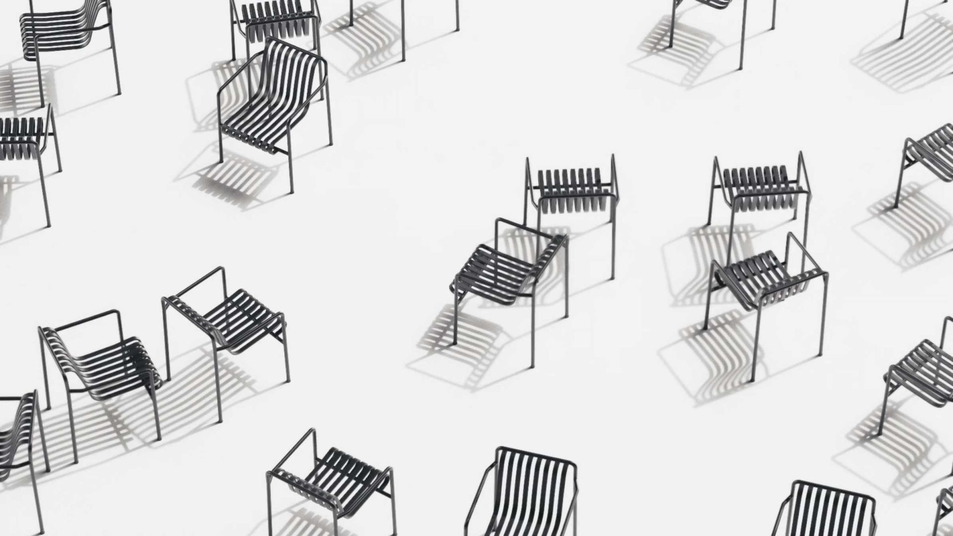 Aerial view of several black metal FRAME chairs with slatted seats and backs, spaced apart on a white surface, casting distinct shadows and highlighting the charm of chairs in minimalist design. Frame from Stash Magazine article.