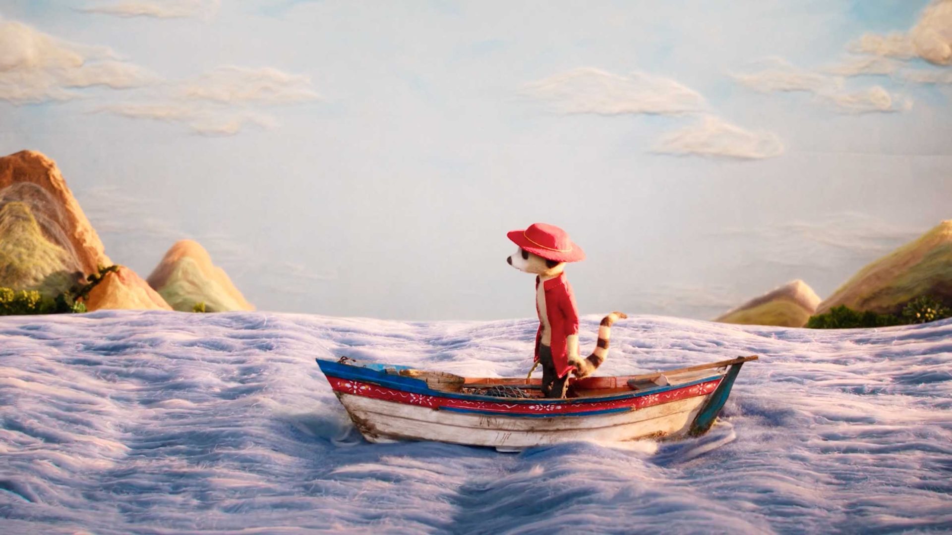A small animal wearing a red hat and jacket stands in a wooden rowboat on wavy blue water, as if The Storyteller in a whimsical tale, with painted hills and clouds in the background. Frame from Stash Magazine article.