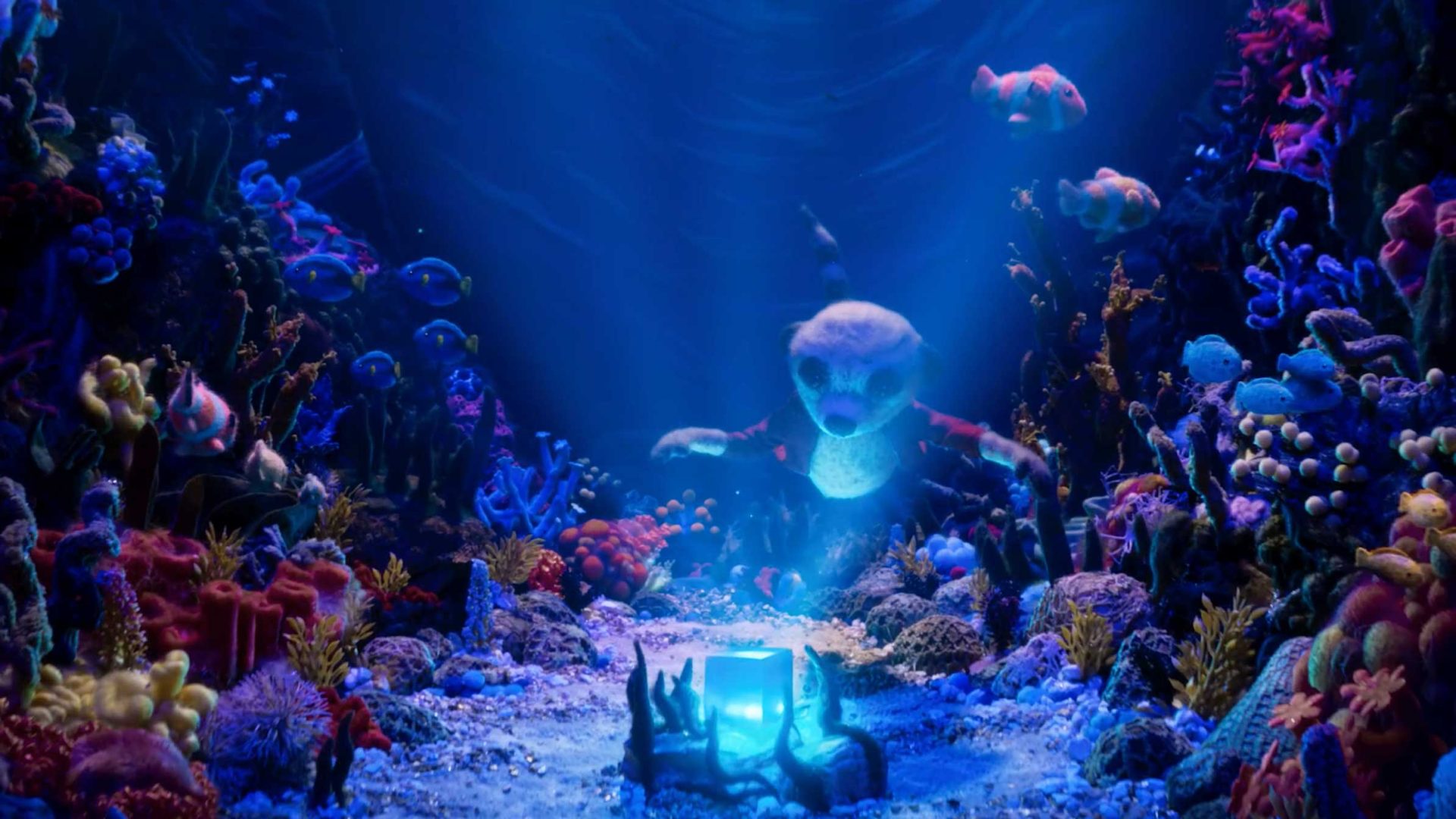 A glowing blue box sits on the ocean floor, surrounded by colorful coral and fish. In this vibrant underwater scene—much like how Zombie & Jungler told the story of The Storyteller for AXA—a shark with big eyes swims toward the box, illuminated by blue light, capturing a sense of wonder and intrigue beneath the waves. Frame from Stash Magazine article.