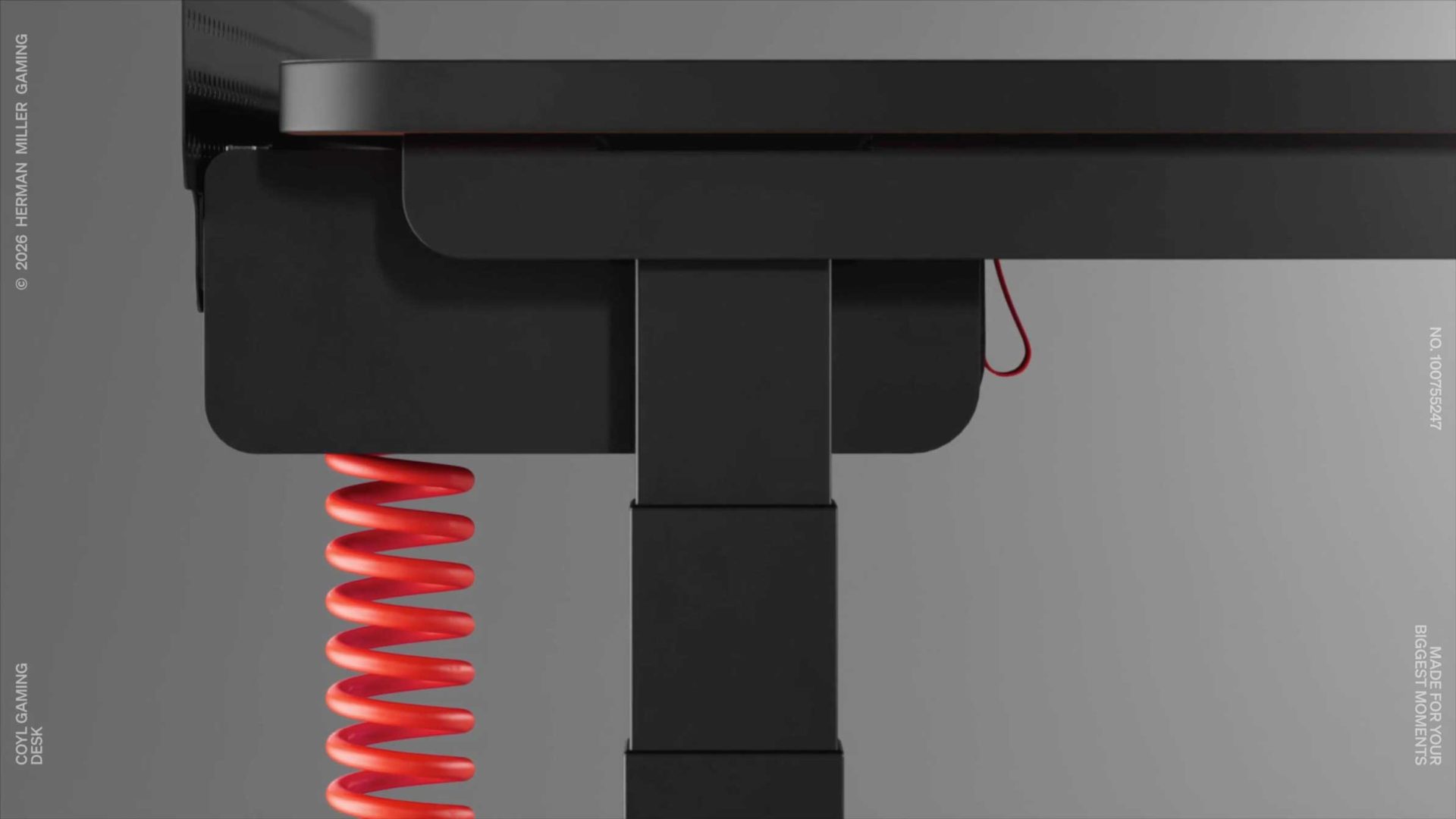 Close-up of a sleek black gaming desk by Herman Miller Gaming, with a red coiled cable hanging underneath and a red clip on the side, showcasing modern and minimalistic design features. Frame from Stash Magazine article.
